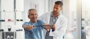 A man smiles as he uses a rubber band for injury recovery treatment under the supervision of his doctor