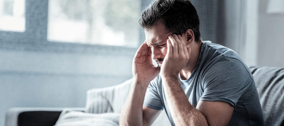 Peripheral Nerve Stimulators for Pain An Overview-3-Ouch A man sits on a couch with his head in his hands due to migraine headaches
