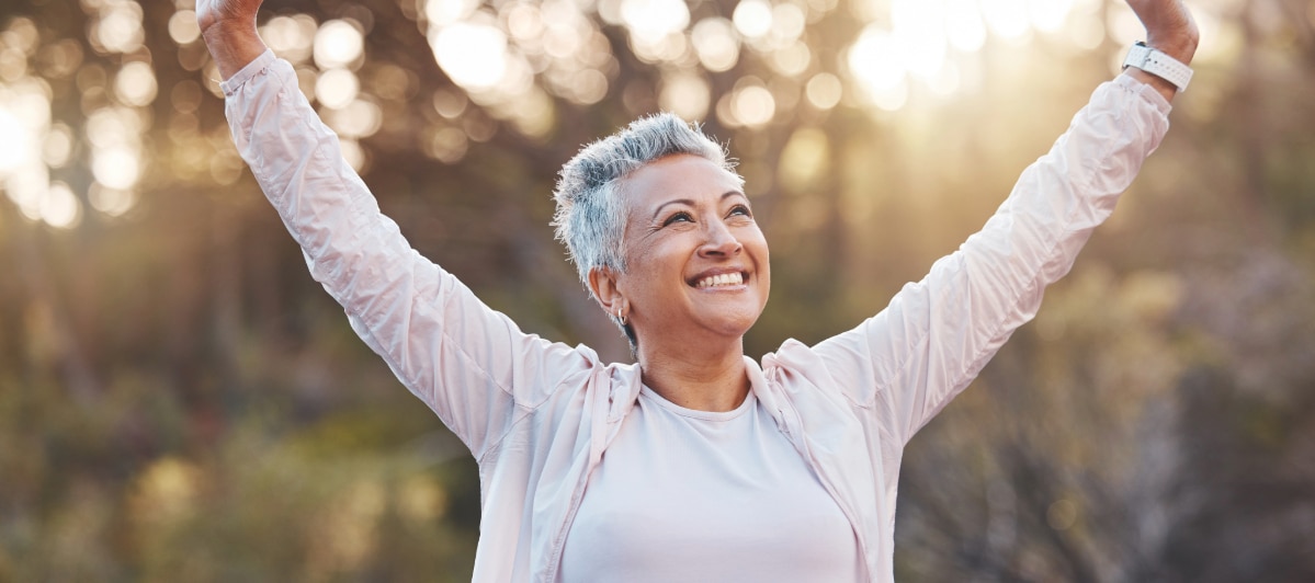 A woman smiles and raises her arms due to improved mobility from sacroiliac joint injections
