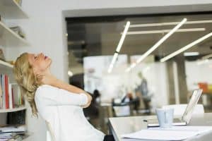 A woman sitting at her desk suffering from neck pain