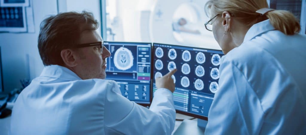 A doctor points to a brain scan image as his colleague looks more closely
