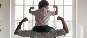 A person flexes his muscles with a child on their shoulders doing the same