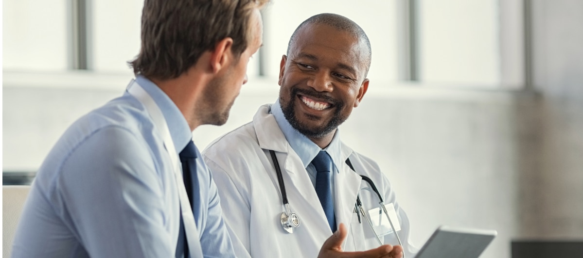 The Best Injections for Neck Pain-6-Smile A doctor in a lab coat smiles as he talks with a colleague about injections for neck pain