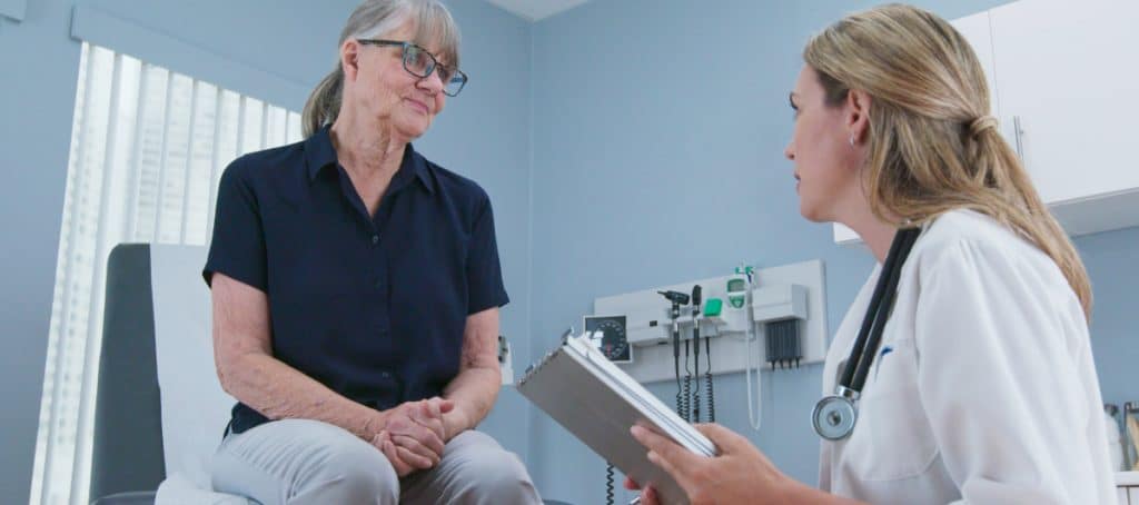 A patient sitting on an exam table listens as her doctor recommends treatment for diabetic neuropathy