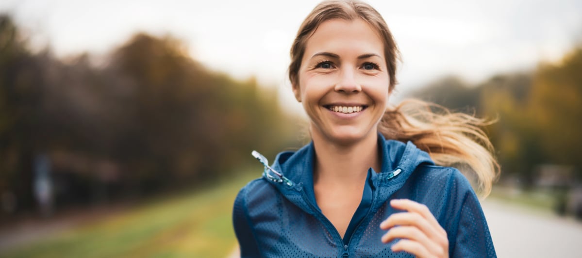 A woman smiles as she jogs on a nature trail to diminish the effects of diabetic neuropathy