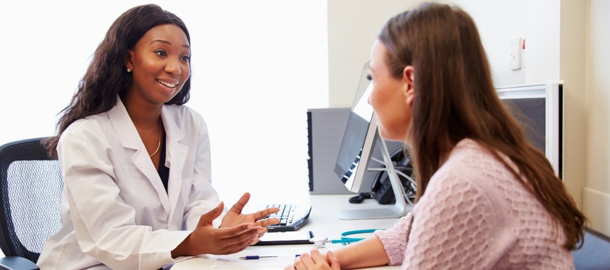 The Relationship Between Inflammation and Weight Gain-6-Doc A doctor in a lab coat smiles as she tells her patient about the link between inflammation and weight gain