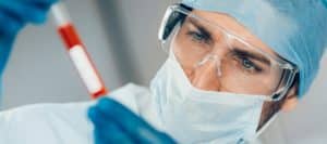 A doctor in full scrubs and exam mask examines a vial of blood during platelet-rich plasma