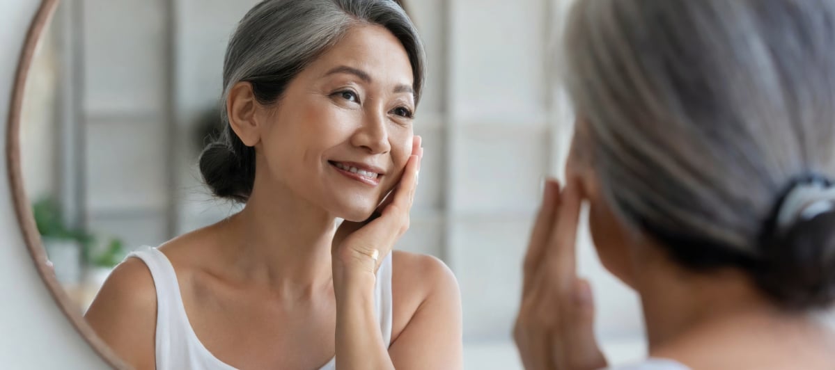 The Science Behind Platelet-Rich Plasma Therapy-4-Face A woman smiles and touches her face as she looks in the mirror after platelet-rich plasma therapy
