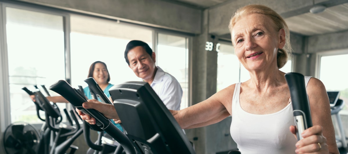 The Science Behind Platelet-Rich Plasma Therapy-8-Gym A older woman smiles as she works out on an elliptical machine at a gym