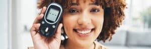 A woman smiles and holds up her digital blood glucose monitoring kit