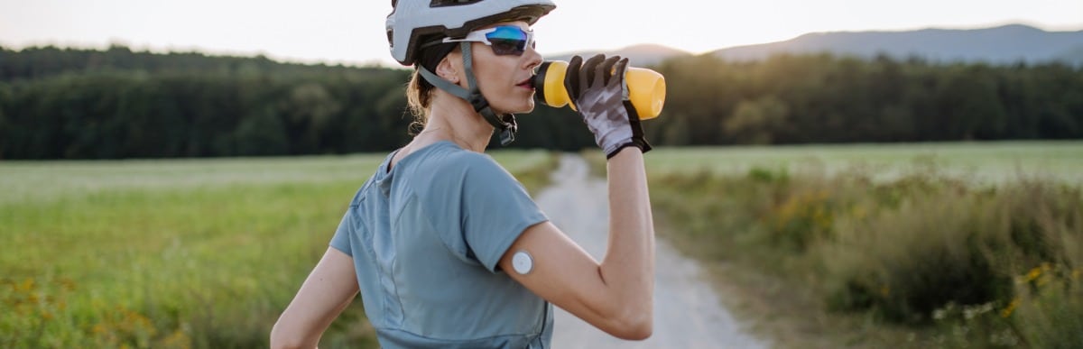 The Ultimate Guide to Blood Glucose Monitoring Kits-4 A cyclist takes a break from her ride to drink water while wearing an arm glucose monitor