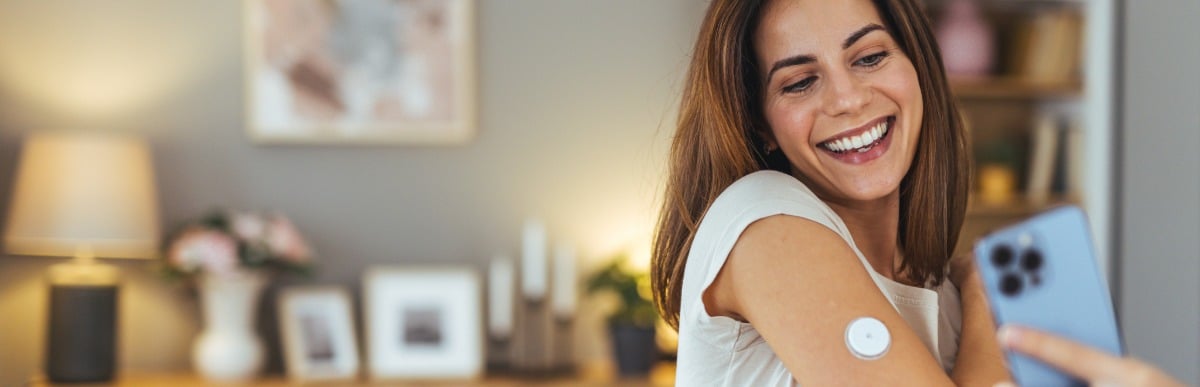 The Ultimate Guide to Blood Glucose Monitoring Kits-6 A woman smiles and takes a selfie of her glucose monitor on her arm