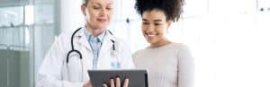 A doctor in a lab coat points to a tablet and tells a patient about Emsculpt Neo treatment