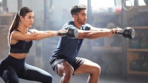A man and a woman exercise with kettle bells after improved health after Emsculpt Neo treatment