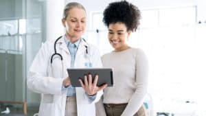 A doctor in a lab coat points to a tablet and talks to a patient about Emsculpt Neo treatment