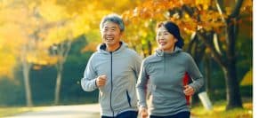An older couple smiles as they jog through the park