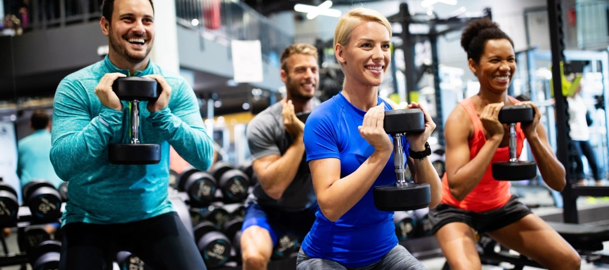 Types of Spine Surgery Explained-5-Gym A group of friends smile as they perform an exercise with weights at a gym