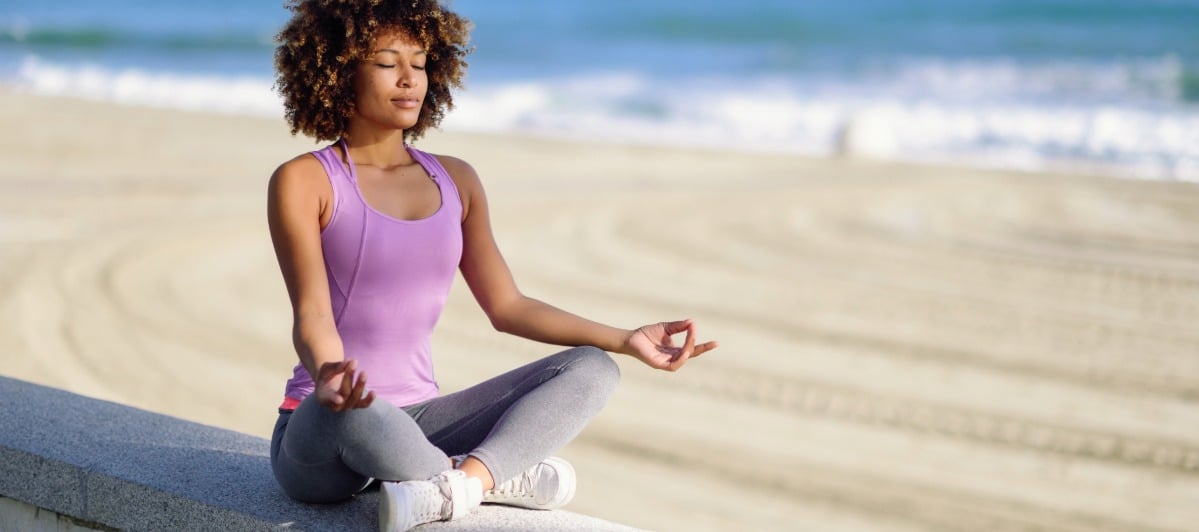 Understanding Spinal Decompression What You Need to Know-5-Peaceful A woman closes her eyes and smiles and she sits and meditates at the beach after spinal decompression