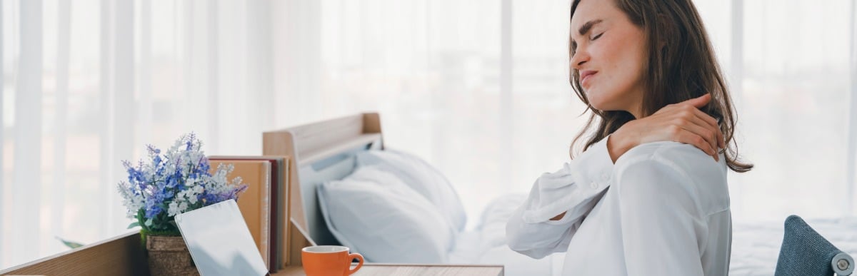 What Is Injection Therapy-2 A woman sitting at a desk winces and holds her upper back in pain before injection therapy