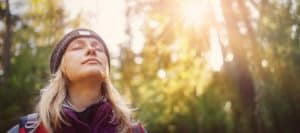A woman closes her eyes and enjoys standing in the woods due to regenerative medicine