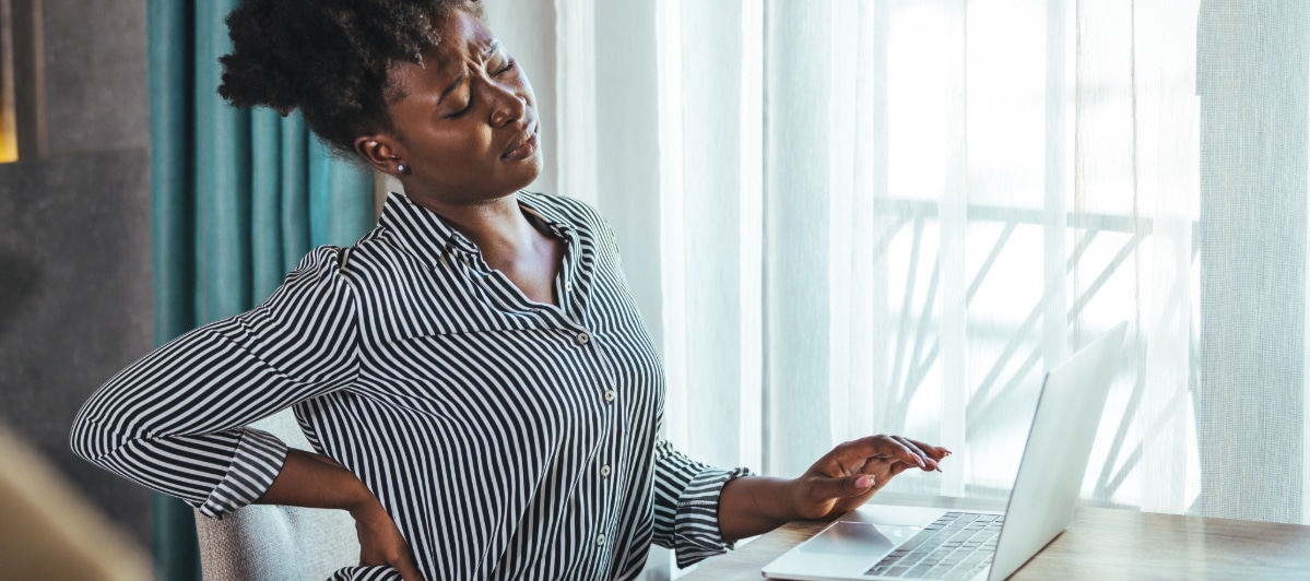 What You Need to Know About Surgical Decompression-3-Pain A woman sitting at a desk winces in pain and holds her back