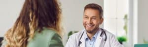 A doctor in a lab coat smiles as he talks with a patient about alternative pain relief