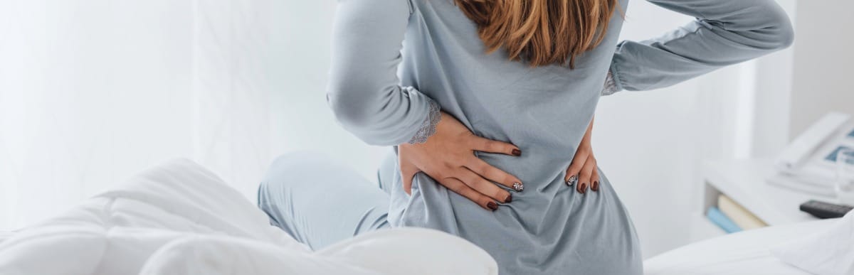 When to Eat to Optimize Health and Wellness-2-Back Pain A woman sits in bed and holds her back due to chronic pain before seeking alternative pain relief