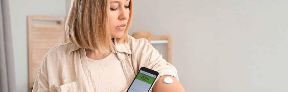 Why Blood Sugar Support Matters at Every Age-2 A woman uses her phone to check a glucose monitor on her arm as part of a blood sugar support plan