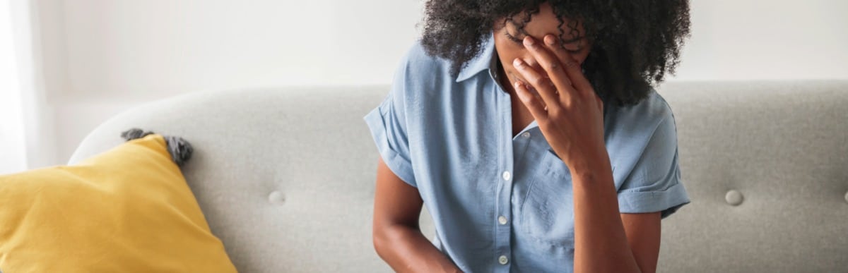Why CGMs Are Changing Diabetes Care-2 A woman sitting on a couch puts her hand to her head as she deals with high glucose levels