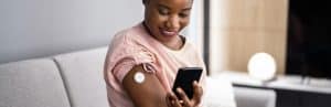 A woman smiles as she uses CGMs to check her glucose level on her phone