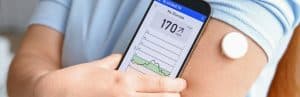 A person with diabetes checks their sugar balance levels with their phone and a glucose monitor