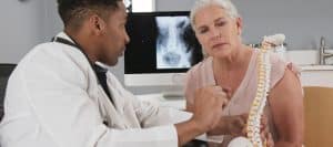 A doctor explaining the source of back pain to a patient with a spine replica